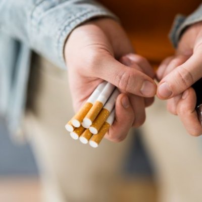 Two hands - one holding a pack of traditional cigarettes, the other holding a vape